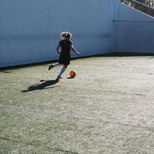 A young woman playing soccer, dribbling a ball on an outdoor field in daylight.